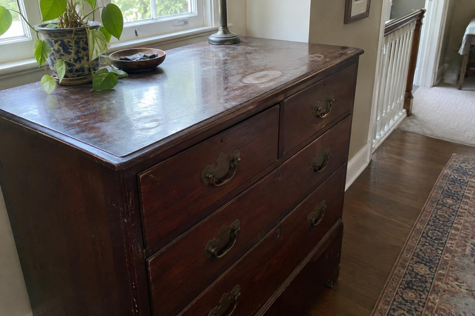 An old mahogany chest of drawers with a dull hazy top, water rings and darkened brass handles