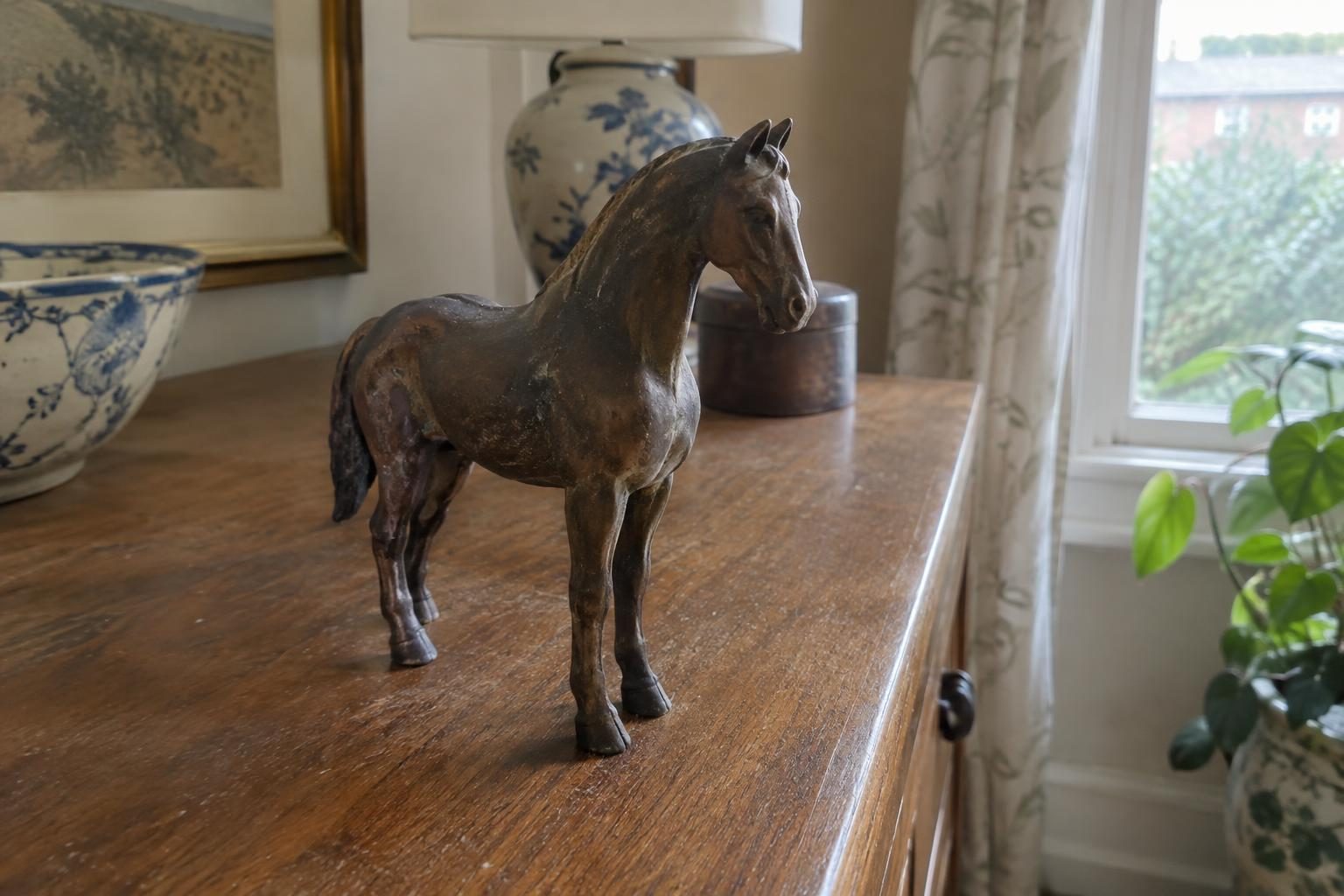 A small bronze horse figure with a deep brown patina standing dusty on a wooden sideboard