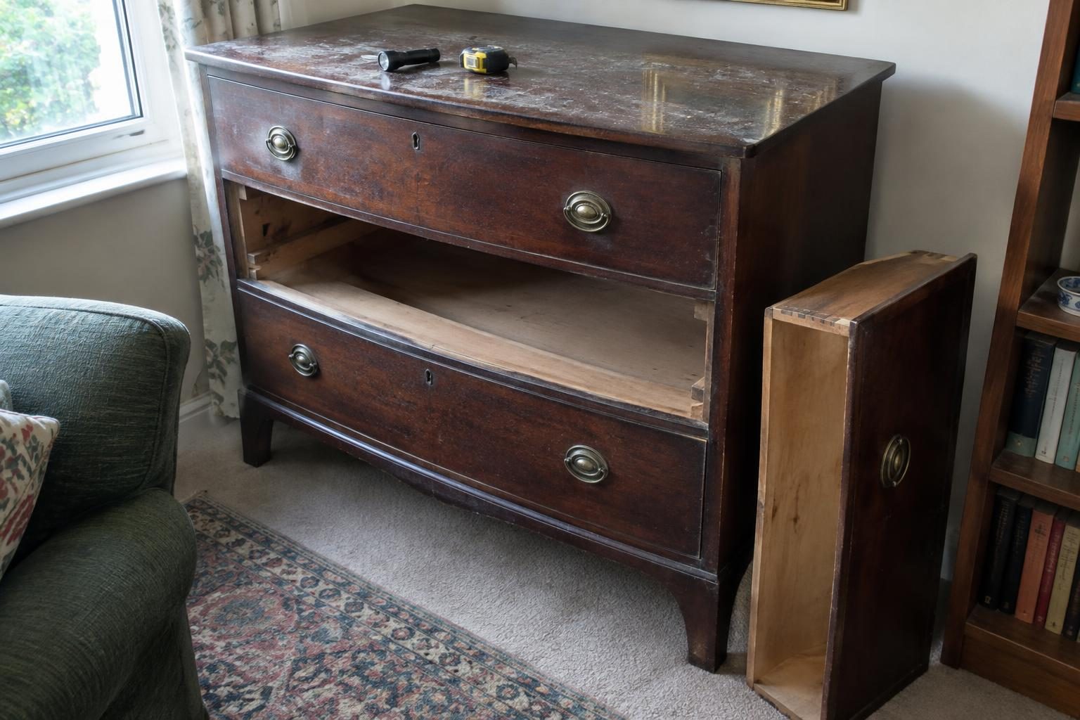An old chest of drawers with one drawer pulled out and standing on the floor, a torch and tape measure on top